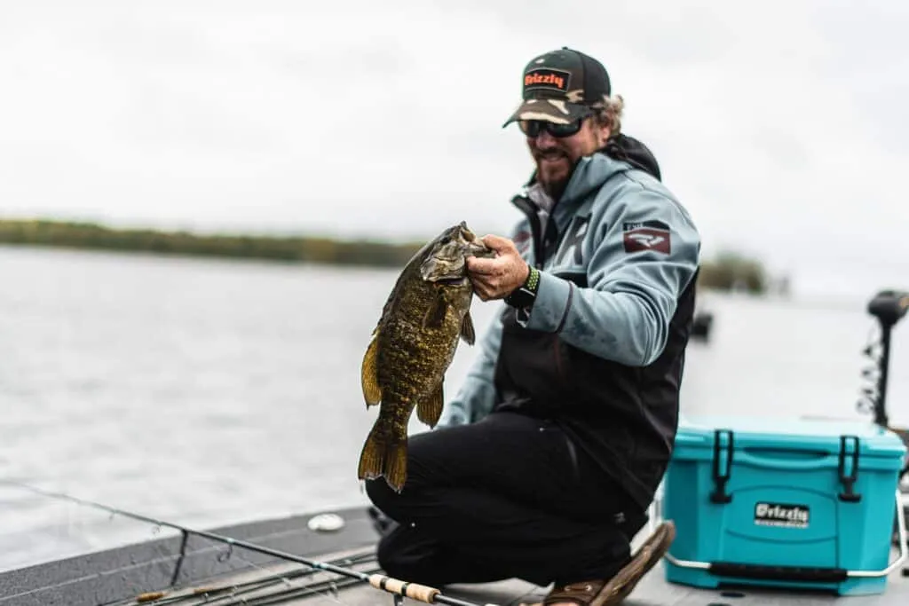 An angler holding up a thick, 5-pound smallmouth bass with the vast, open water of Mille Lacs in the background.